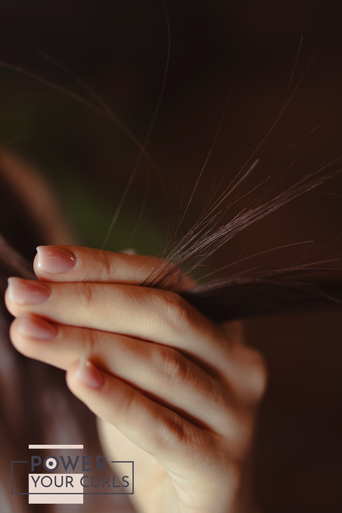 A close-up of a woman’s hand, holding the end of her hair in between her fingers.