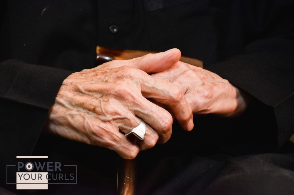 Old, wrinkled hands holding onto a cane.