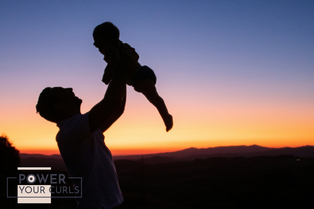 A silhouette of a man lifting his young son with a sunset in the background.