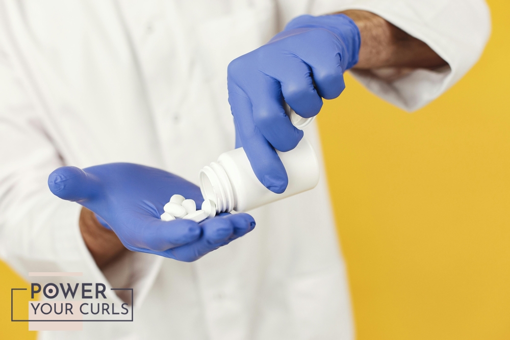 A close up photo of a man wearing a lab coat and latex gloves, pouring tablets from a bottle into his hand.