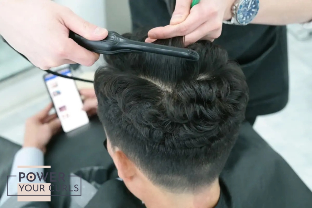 A man getting his hair permed with a curling iron at a salon.