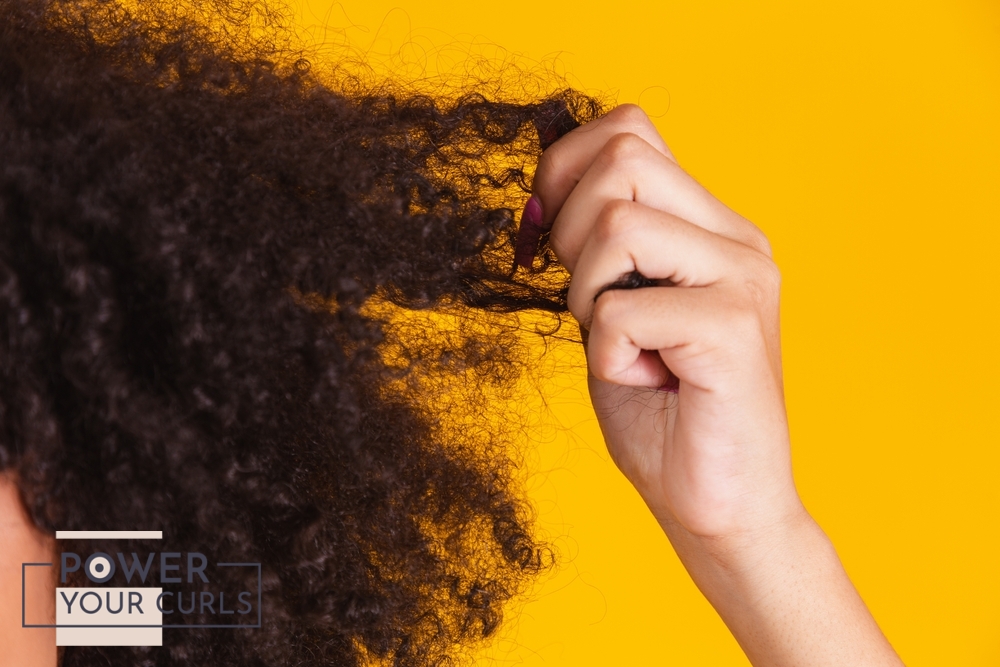 A hand pulling at frizzy, curly hair.