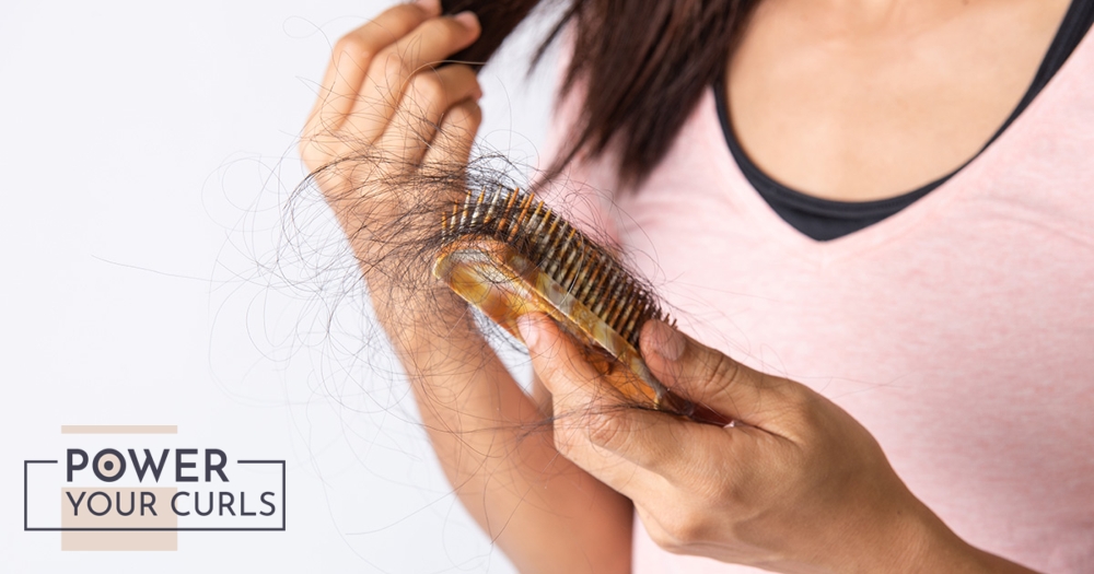 A woman holding a hair brush filled with hair strands.