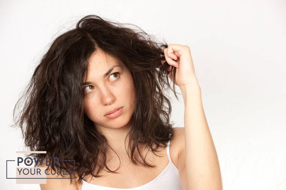 A concerned looking woman holding her limp hair in her hand.