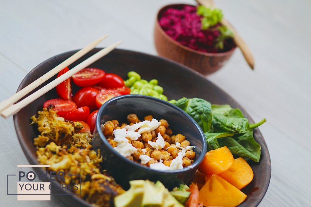 A large bowl filled with a healthy meal of fruits and vegetables, beside it is a smaller bowl filled with what looks like purple rice.