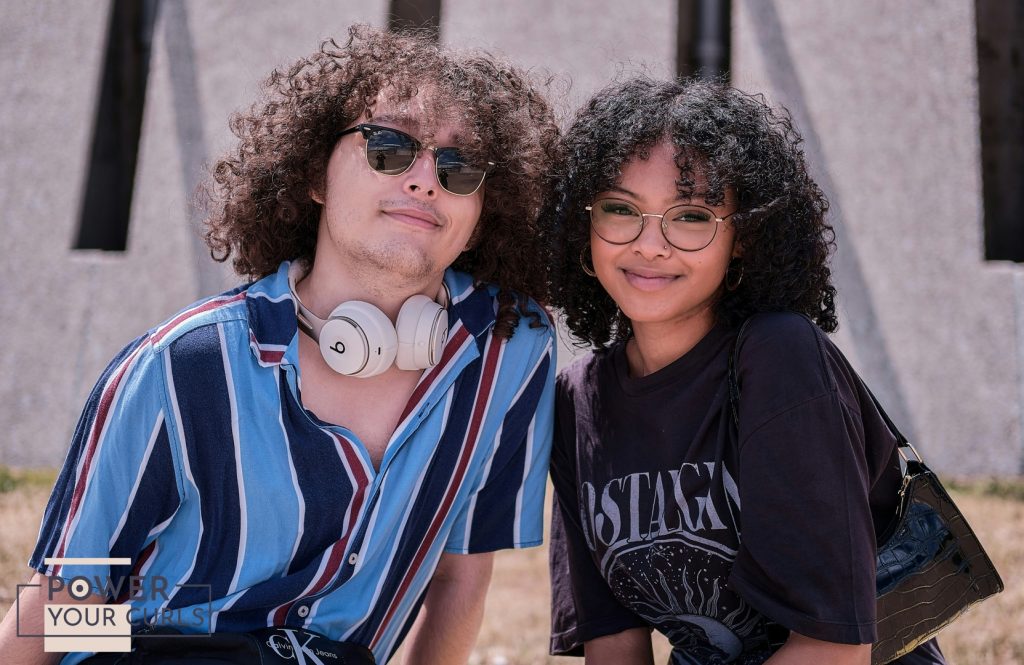 A young man and woman, both with curly hair, smiling for the camera.