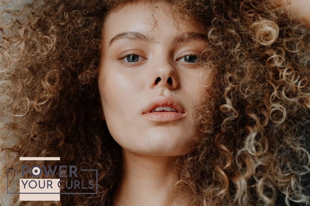 Why Is My Curly Hair Dry? Causes, Signs, and How to Fix It 1 Image of a woman with brown and blonde curls and blue eyes staring straight to the camera